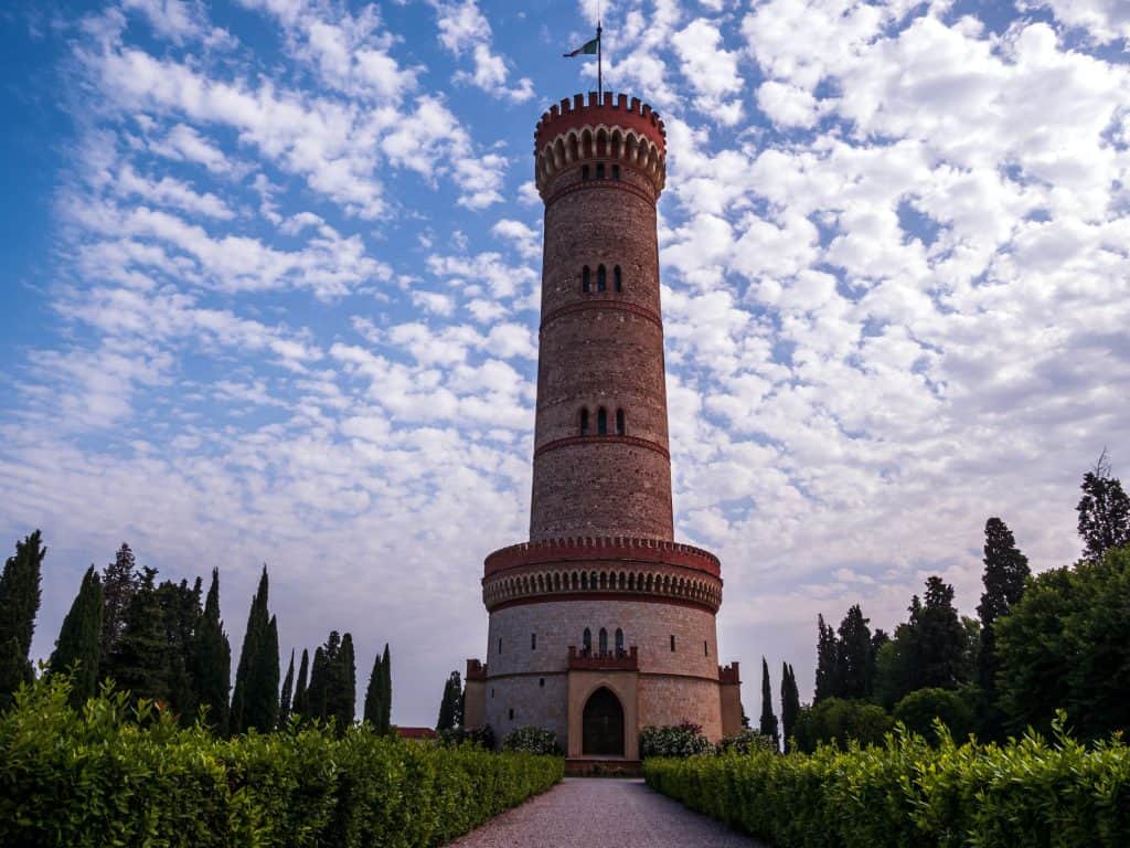 Turreted tower of Torre di San Martino with white and blue sky and gardens in the background