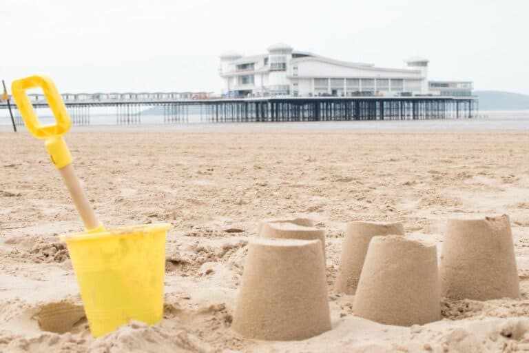 Bucket and spade with sandcastles on a beach with The Grand Pier in the background