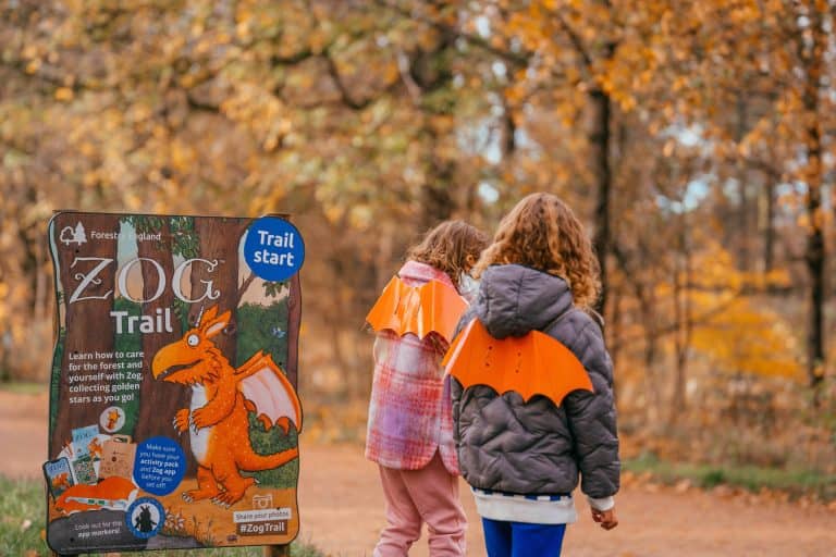 Two children wear orange Zog wings looking away from the camera into the forest