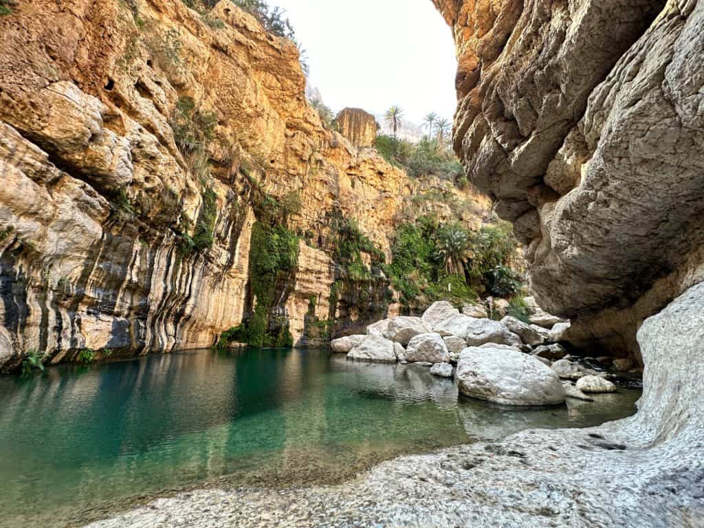 Clear turquoise water of Wadi Tiwi with rocky canyon walls rising on either side