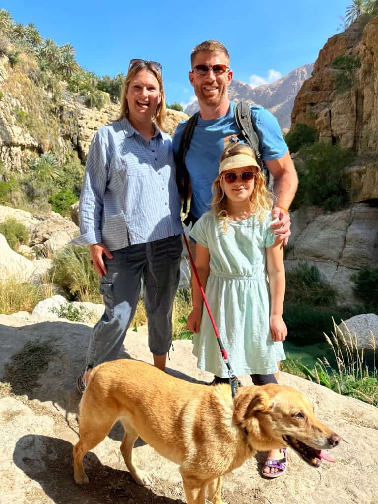 Claire, Mr Tin Box, their seven-year-old and their dog pose for a picture in front of the canyon. The Wadi Tiwi pool they are heading for is visible on the right