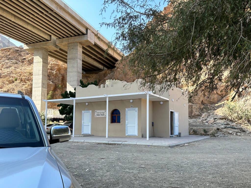 Sand coloured public toilet building in the shade of the Wadi Tiwi viaduct