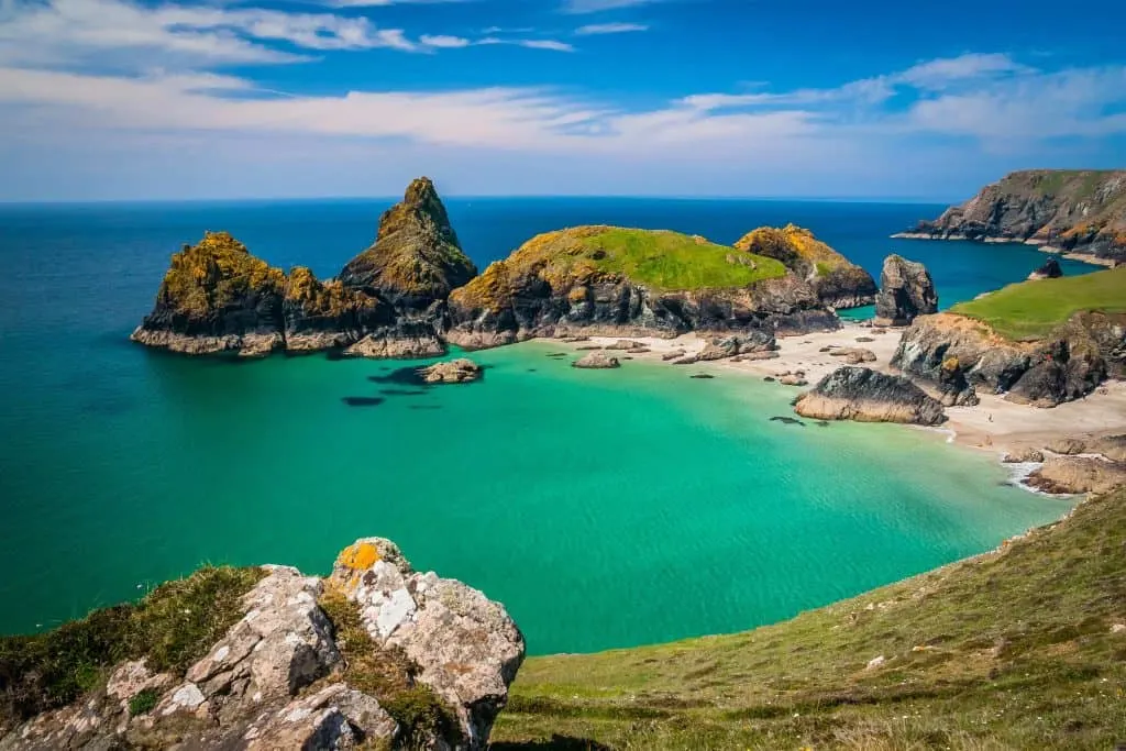 A rocky cove filled with turquoise water edged with a sandy beach on s sunny day