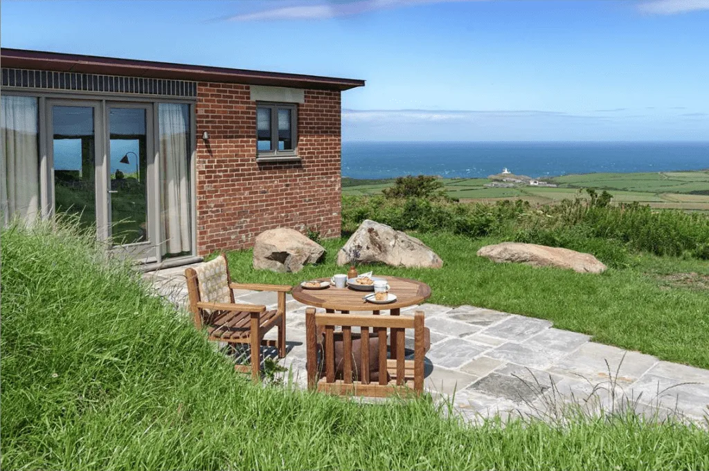 Brick cottage and table and chairs sat in front of a view of the Welsh coast on a sunny day