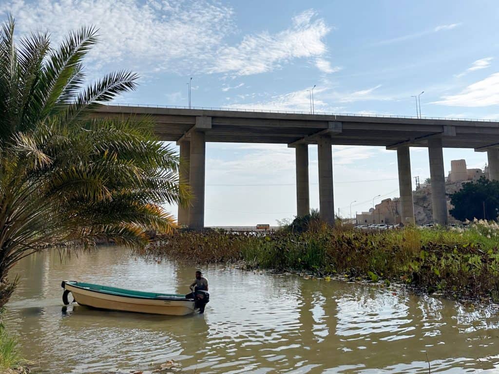 Small motorboat with driver at the entrance to Wadi Shab with viaduct in the background
