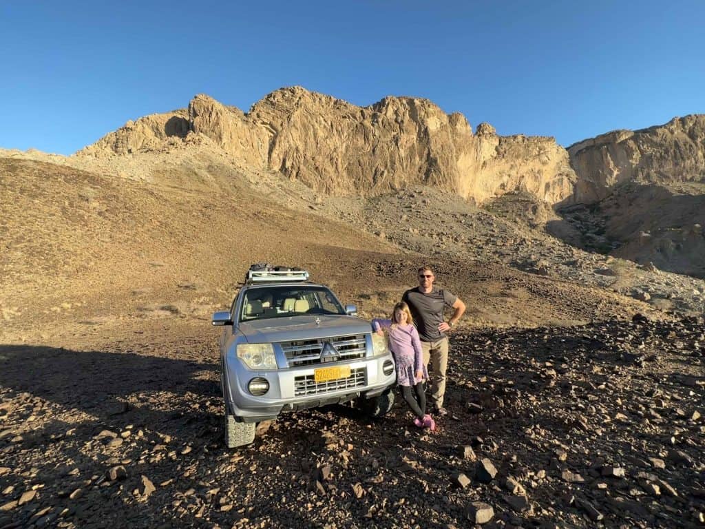 Father and daughter stand with Mitsubishi Pajero 4x4 vehicle in the rocky foothills of Jebel Shams in Oman