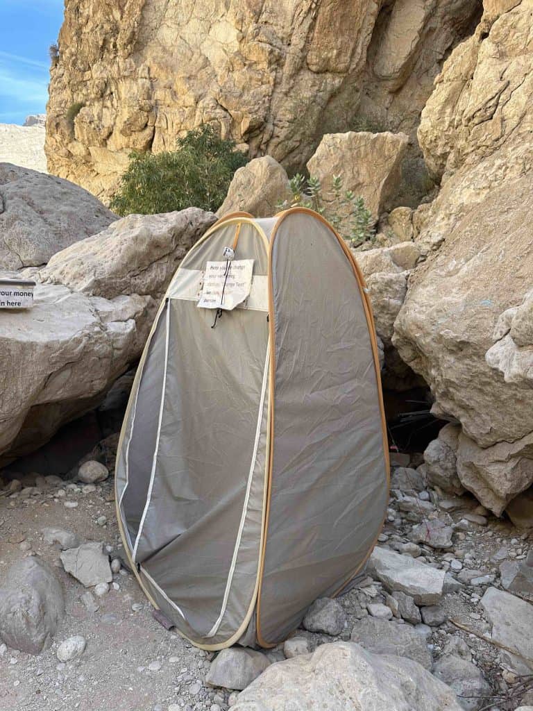 A tall brown toilet tent with a printed sign on the front instructing people to use it to change