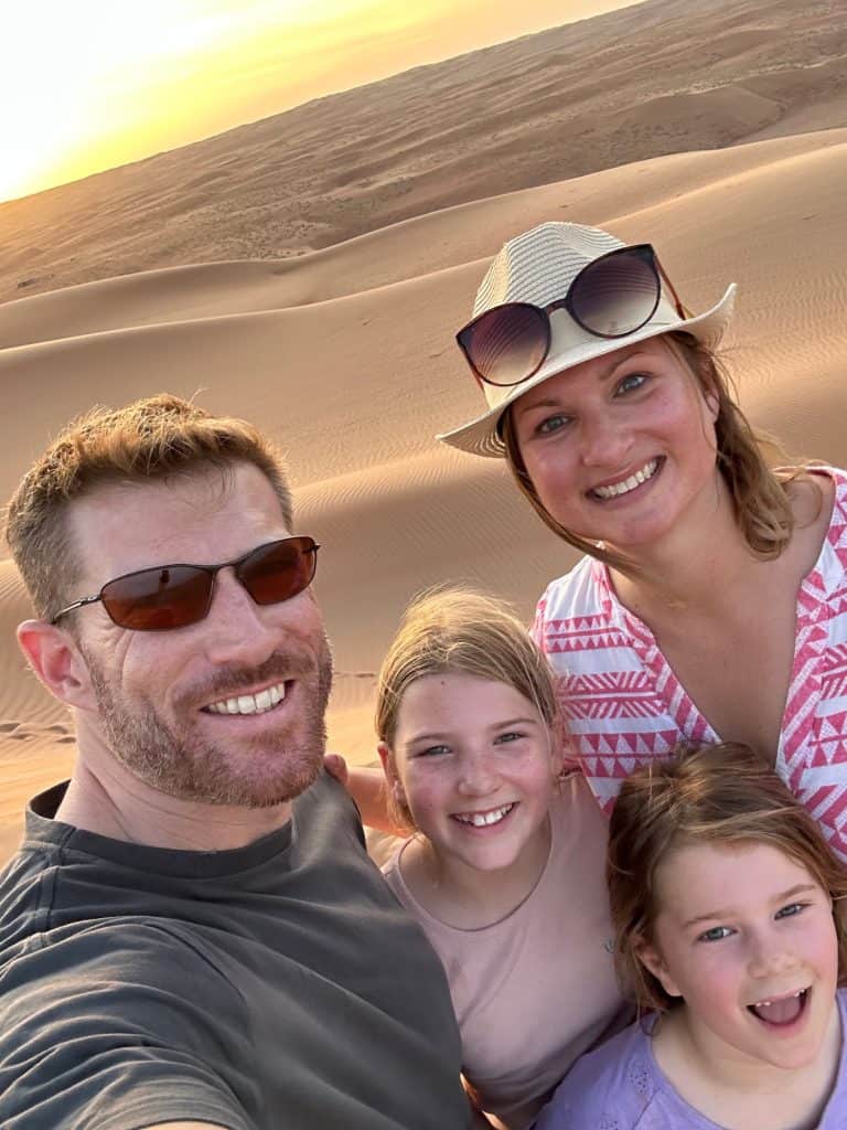 Tin Box family smiles at camera against a backdrop of sunset at Wahiba Sands in Oman