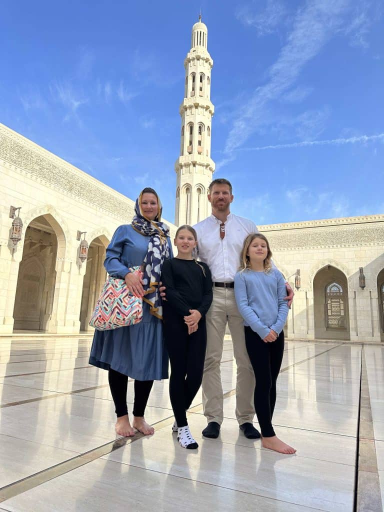 Family stands in marble courtyard of the Sultan Qaboos Grand Mosque in Muscat. They were conservative clothes covering their arms and legs.