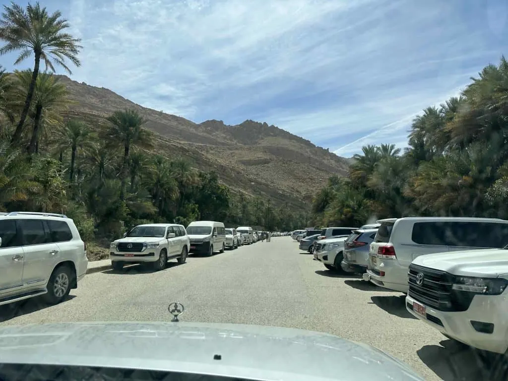 Photo taken through the front windscreen of our car as we drive thought the parking area at Wadi Bani Khalid. Bot sides of the car park are lined with vehicles