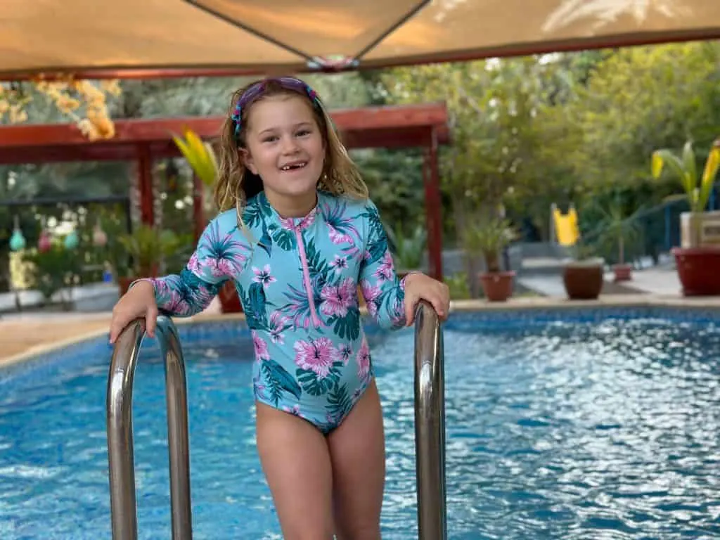 Smiling seven year old girl in brightly coloured swim suit steps out of a swimming pool at Valley Cliff Inn