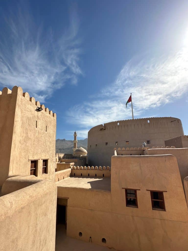 The sandstone castle walls of Nizwa designed in Arabic style with the Omani flag flying from the top of the fort