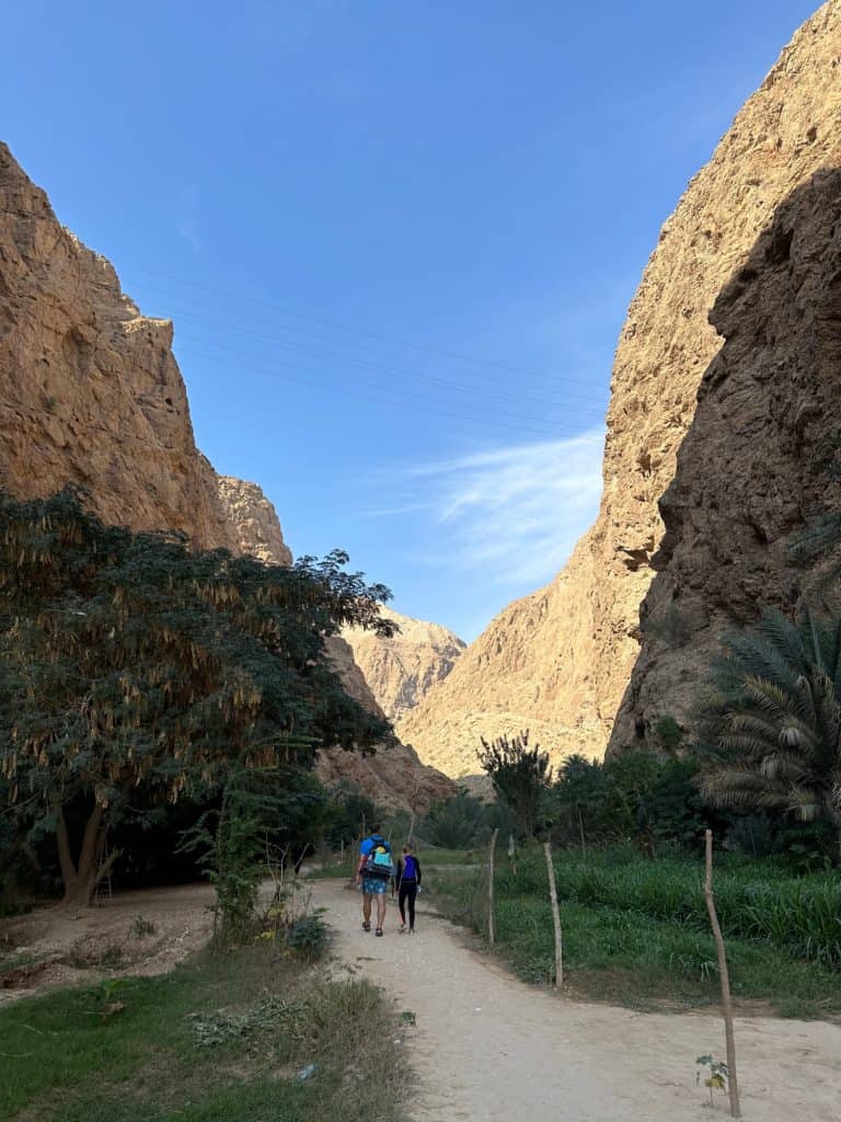Father and daughter walk up the wadi between plantations with the walls of the wadi towering on either side