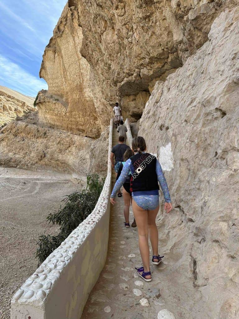 Girl wearing a buoyancy aid and swimwear walks up a concrete ramp built into the side of the valley wall