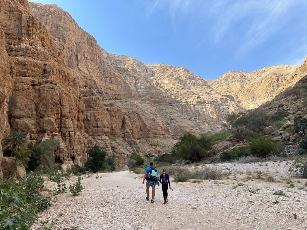 Father and daughter walk up the wadi along a wide shingle path with the walls of the wadi towering on either side