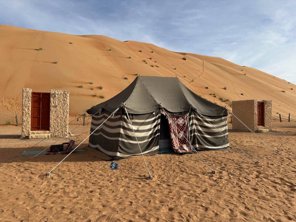 Traditional bedouin black and white striped tent in the orange sands of Wahiba Sands desert