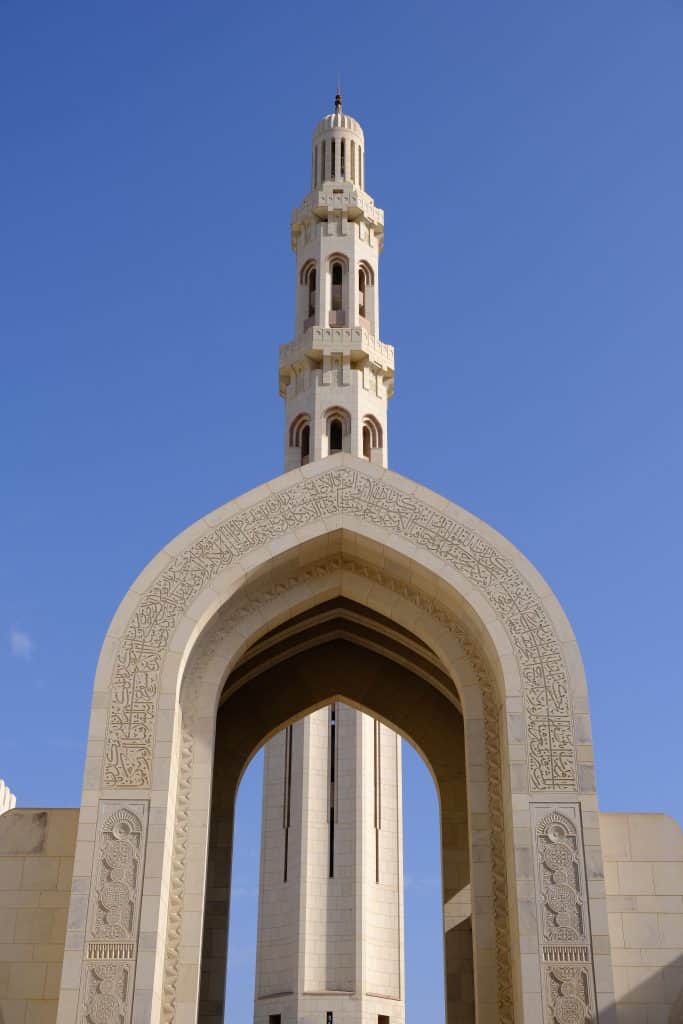 A sandstone archway decorated with Arabic script with the tallest minaret in the background