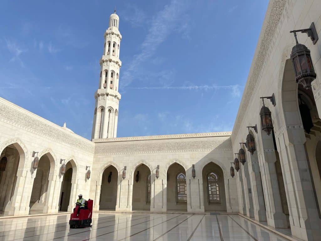A ride on floor cleaner is being driven around a marble courtyard at the Grand Mosque