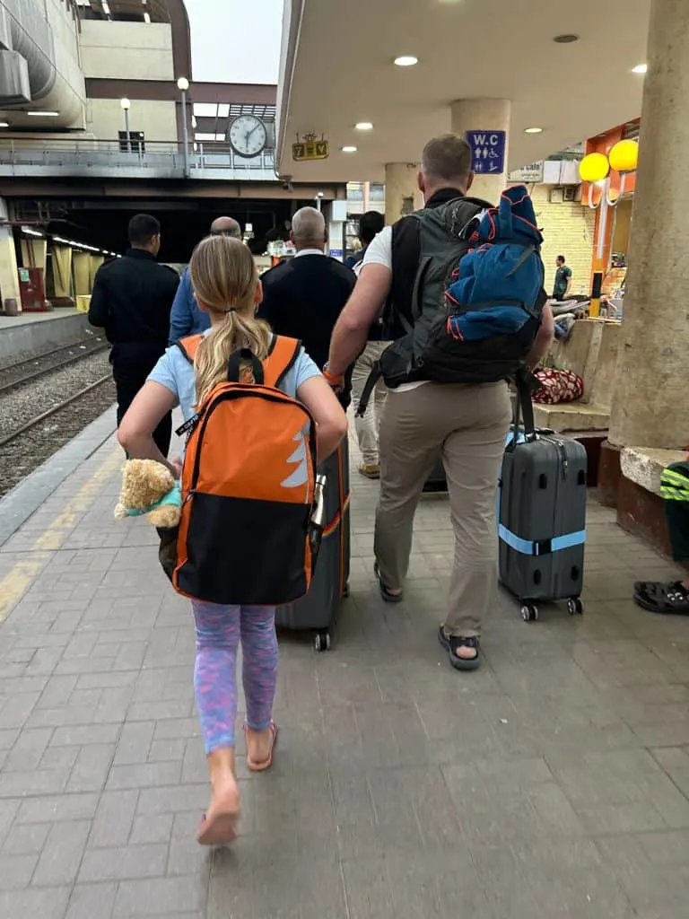Family wheeling luggage onto the station platform at El Giza station. Walking in front of them there are security guards