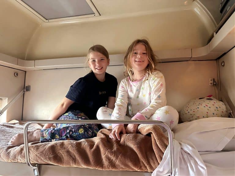 Two girls sat on the top bunk of the sleeper train. They are dressing in pyjamas an smiling