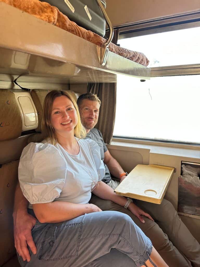 Claire and husband sat in sleeper train cabin in the morning. They look tired