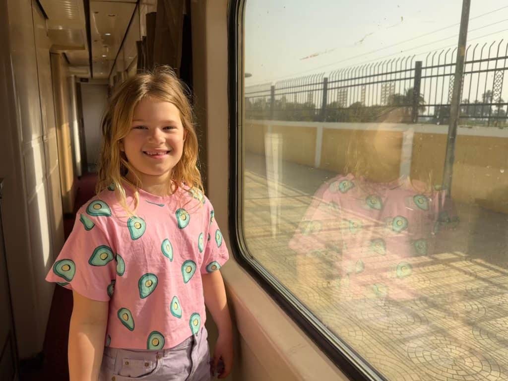Eight year old girl stood by the window in the corridor of the sleeper train which is at a station