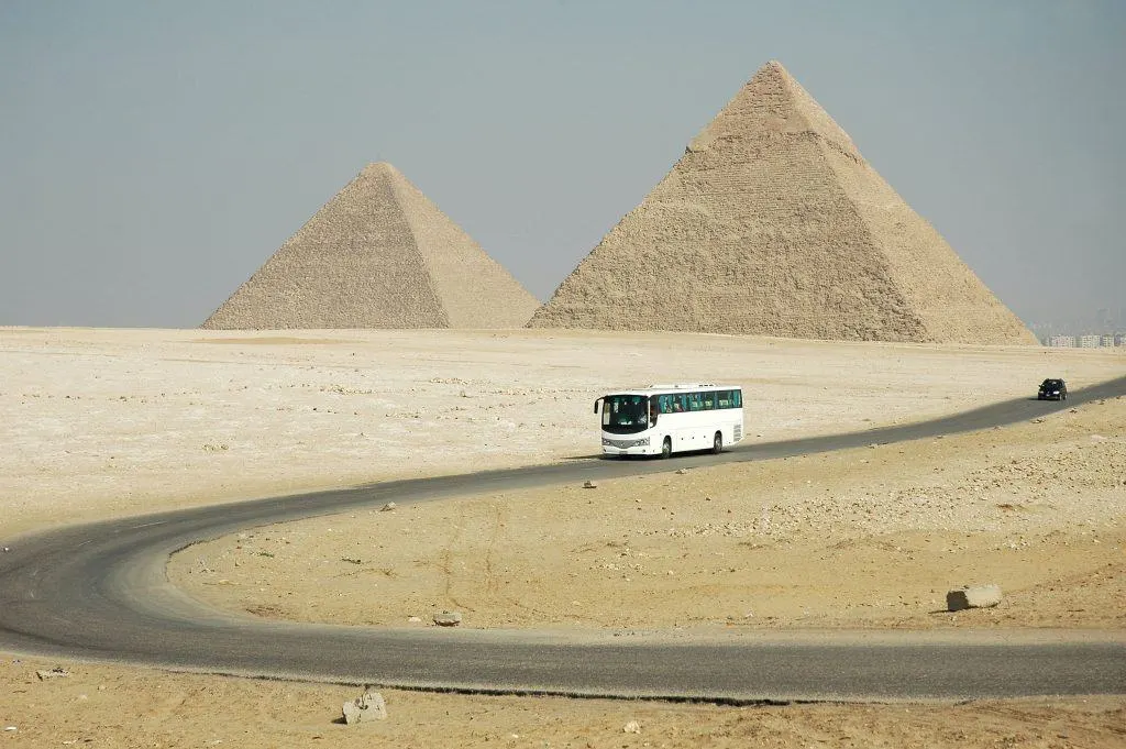 White bus driving down road away from the Pyramids of Giza