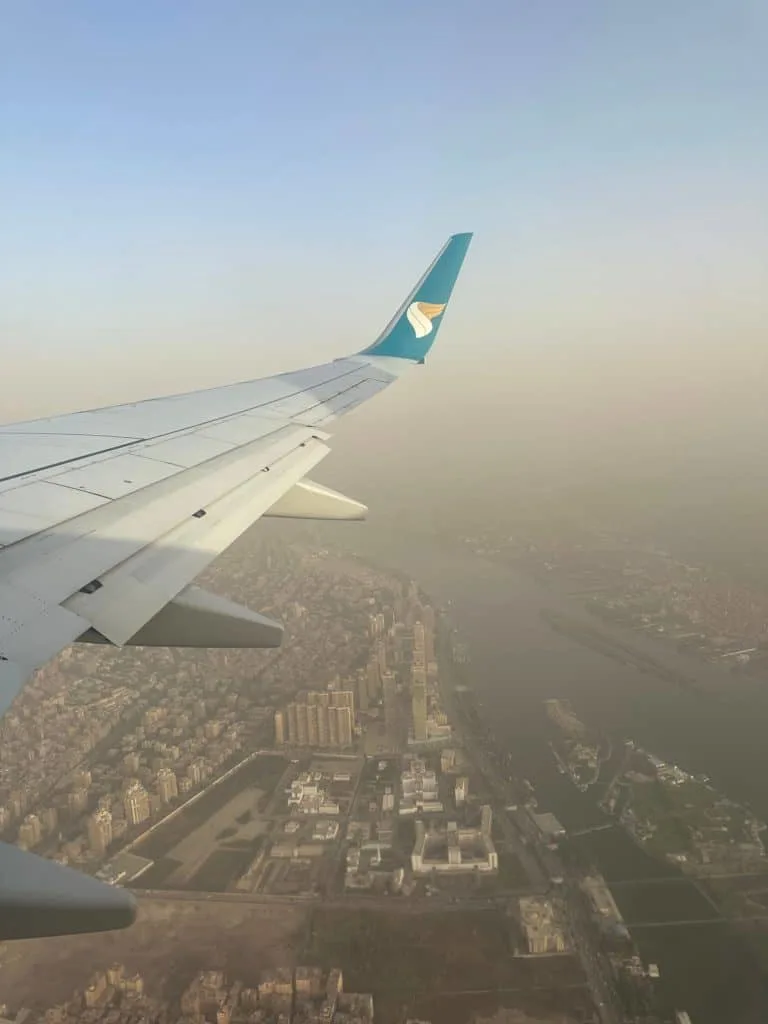Wing of an Oman Air plane with view of a smoggy Cairo city and the Nile below
