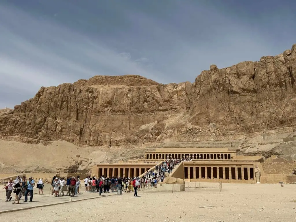 Visitors walk towards Deir Al-Bahari - the temple built by Hatshepsut in the vide of a sandstone cliff. The table has three tiers held up with columns