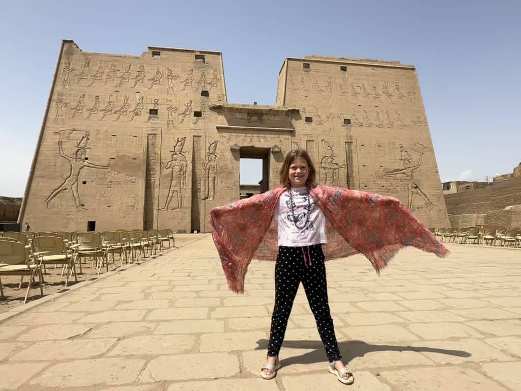 Girl with scarf around her arms stood in front of the walls of Edfu temple