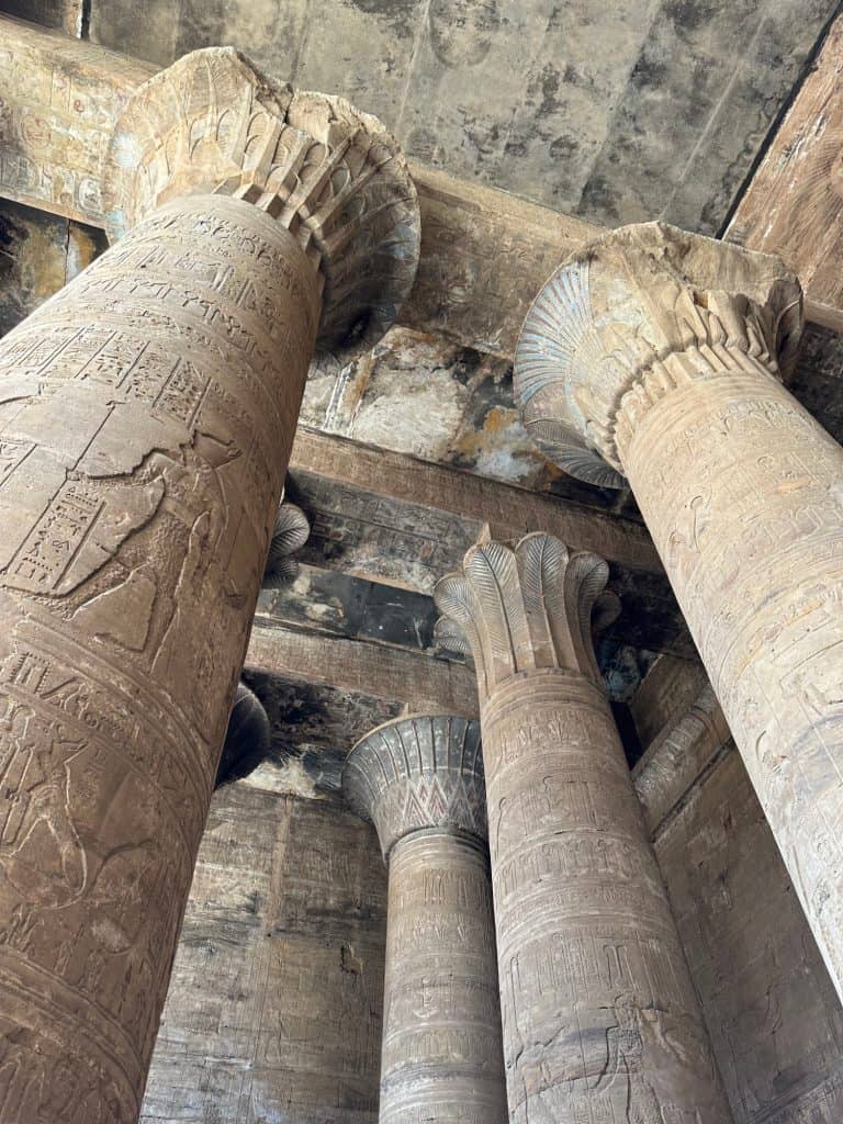 A shot looking up at the tops of the columns in Edfu temple. They are decorated with hieroglyphs and have flower bud-like tops supporting a blackened ceiling