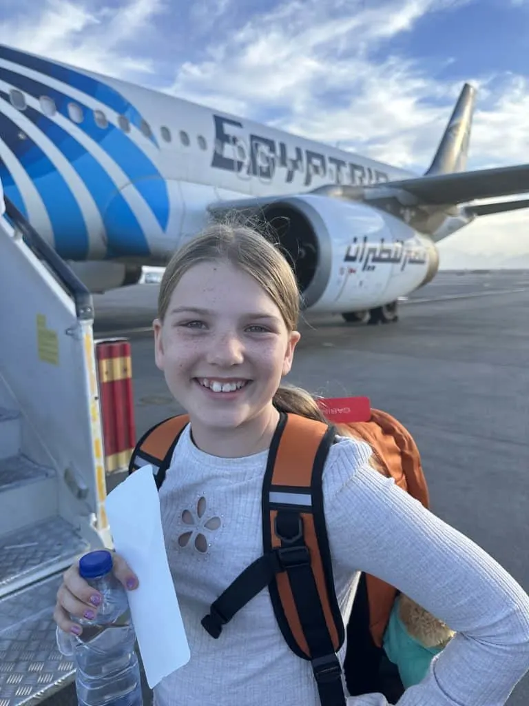 Ten year old girl about to board a fight with Egypt Air. The tail of the plane is behind her. She is holding her ticket