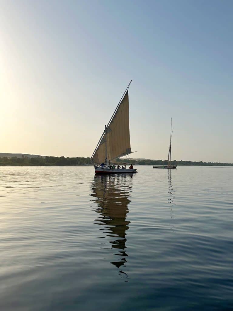 A traditional felucca sailing boat on the River Nile at sun set. It reflects on the water