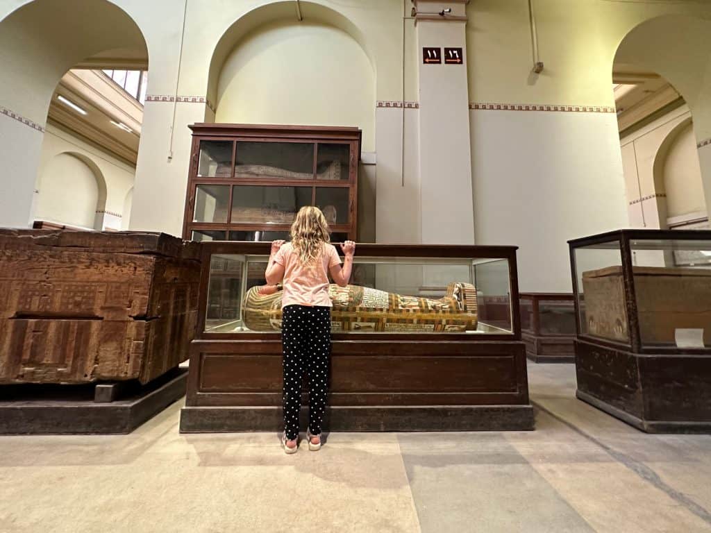 Girl looking at a glass case containing the sarcophagus in the Egyptian Museum