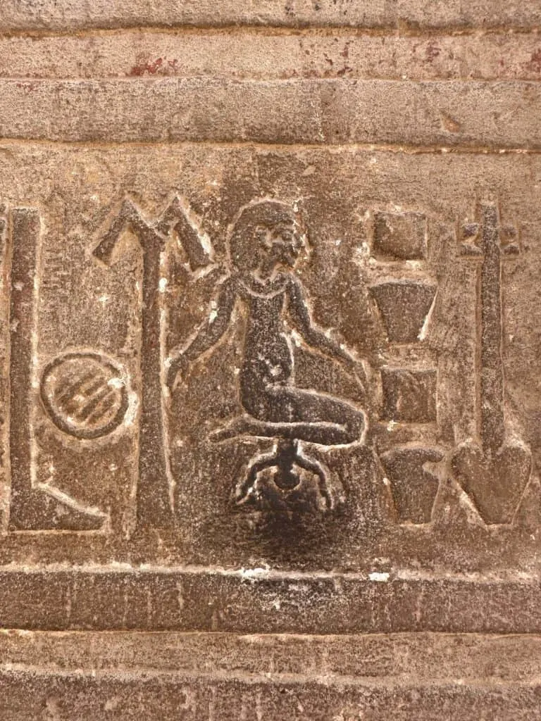Hieroglyph of a woman giving birth to a baby. The carving is dark with finger prints of visitors who have touched it for luck