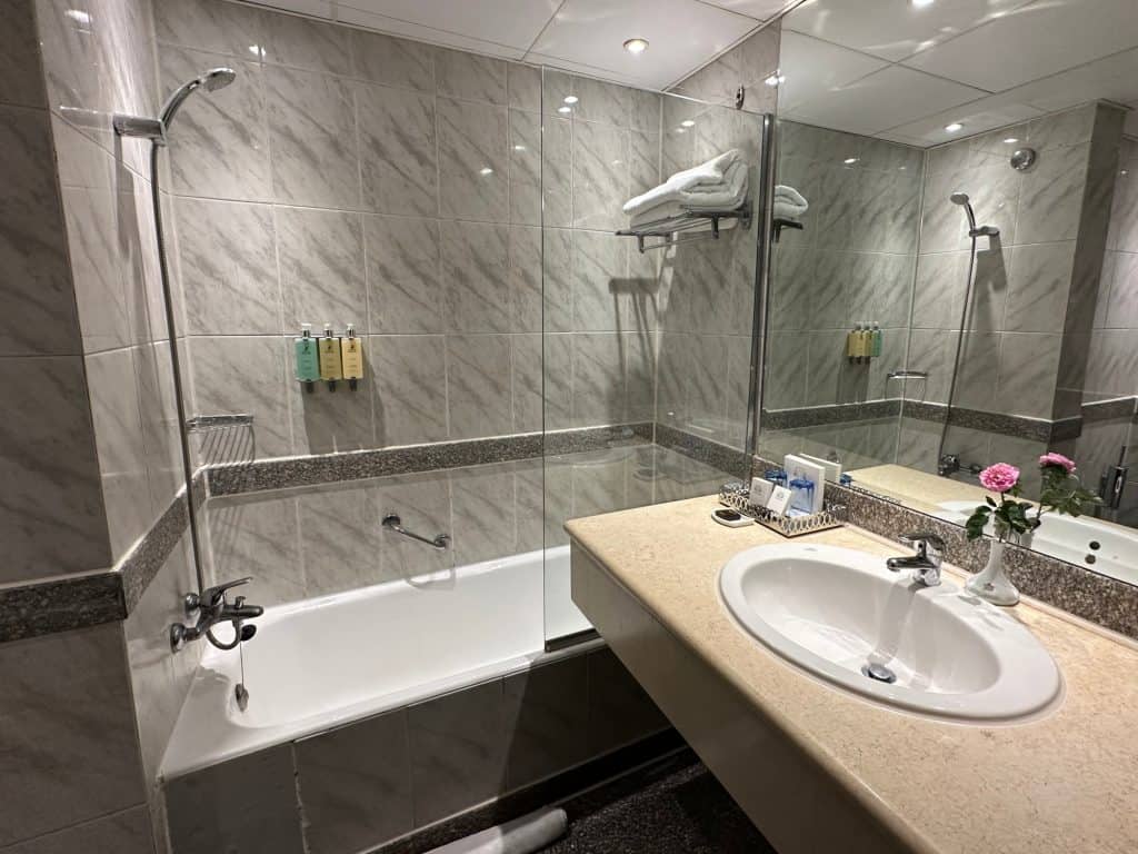 A hotel bathroom where the shower screen is at the opposite end of the bath to the shower head