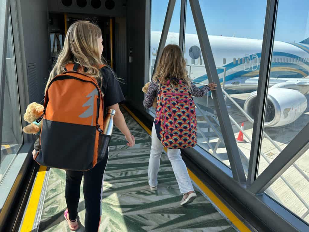 Our daughters walking through the tunnel to a plane wearing back packs