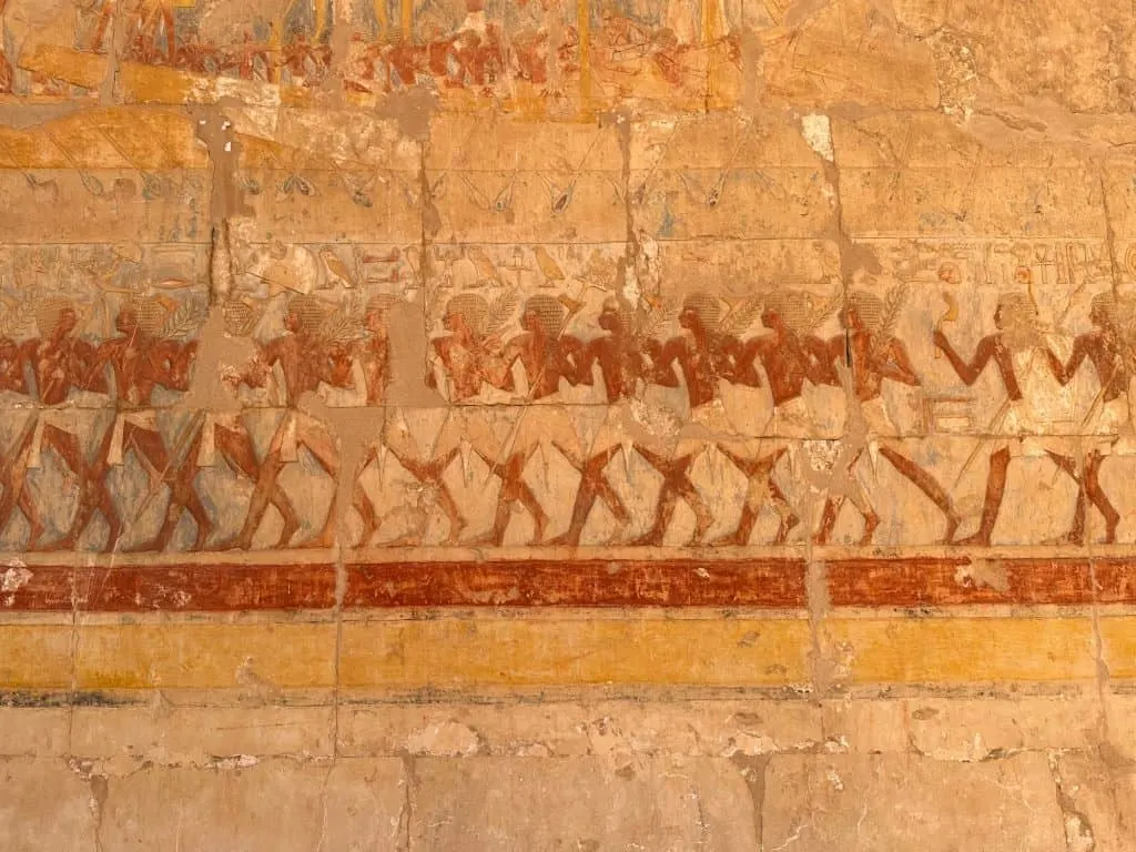 Hieroglyphs showing a row of ancient Egyptians in Deir Al-Bahari temple. The ochre and yellow colours have been preserved