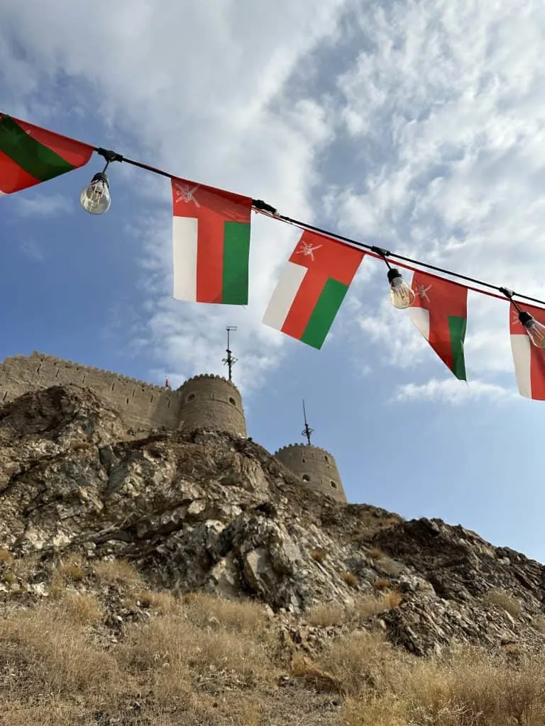 A string of Omani flags flying in front of the towers of Muttrah Fort in Muscat