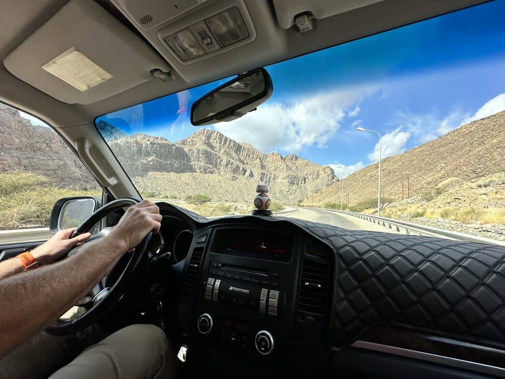 Photo of the view of Jabal Akhdar mountain through the full windscreen of our car. In the foreground you can see the dash board and steering wheel