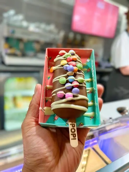 Chocolate ice lolly covered in white chocolate drizzle and multi-coloured sweets