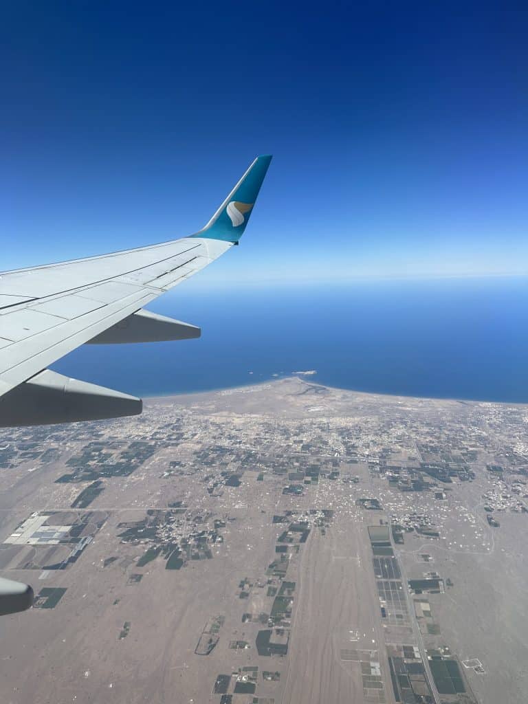 Oman Air plane wing against background of blue sky and the Oman coastline