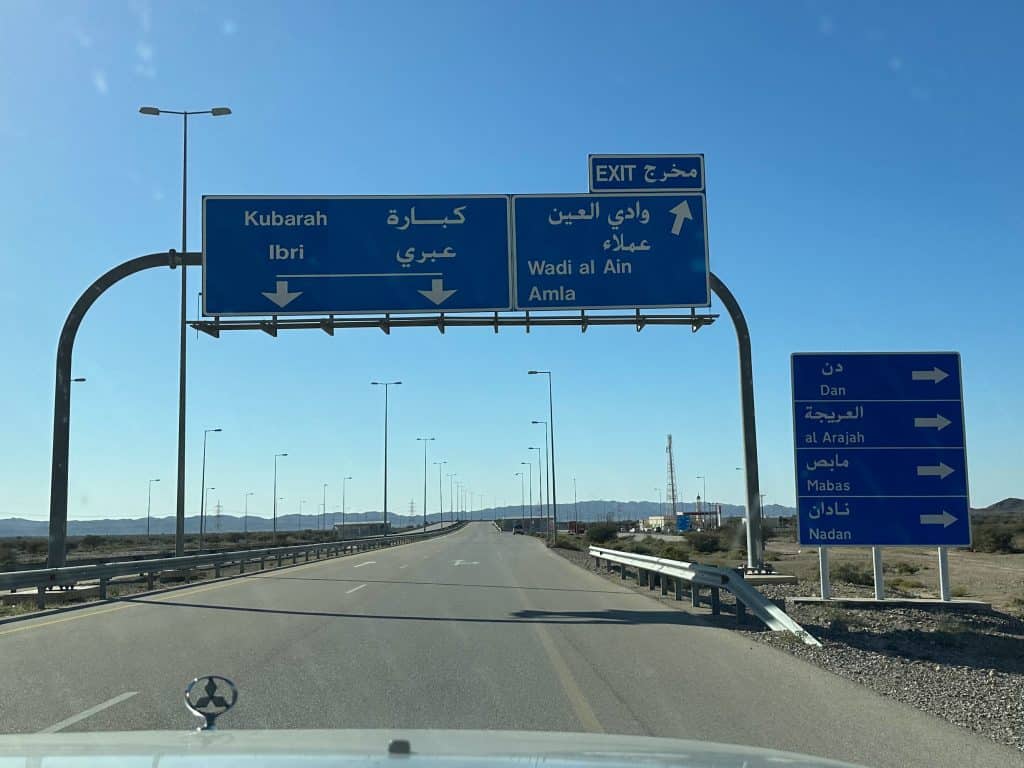 Photo from front seat of car while towards road signs written in English and Arabic