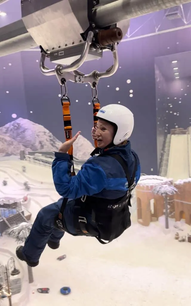 Claire hanging in the harness seat on the Bullet Ride. She is wearing a white helmet and blue show suit