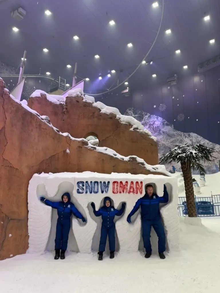 Family standing inside human shaped snow holes with'Snow Oman' written in blue and red above