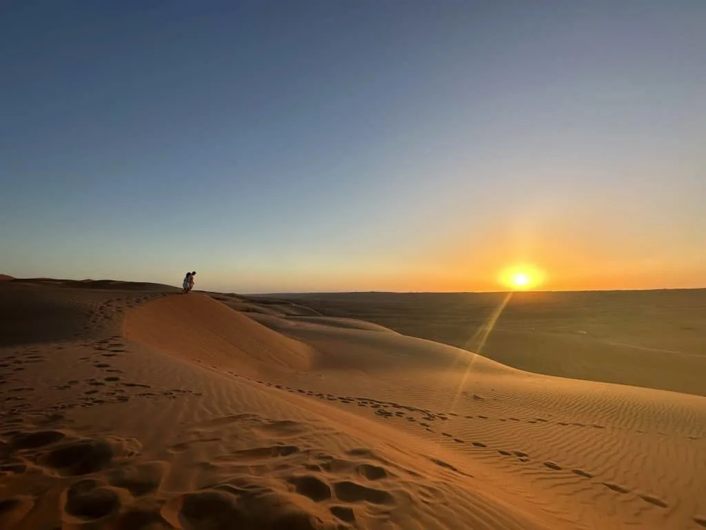 Children stood at the top of a sand dune during sunset over Wahiba Sands in Oman