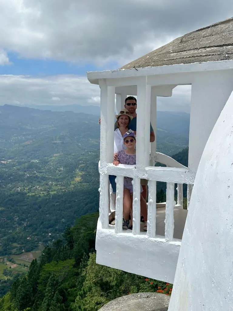 Claire, Mr Tin Box and eight year old stood in balcony on the side of the white washed Ambuluwawa Tower with views of the hills around them