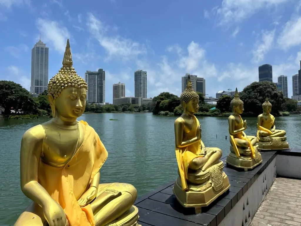 Golden Buddhas sat outside Seema Malaka on the lake in Colombo with modern tower blocks in the background