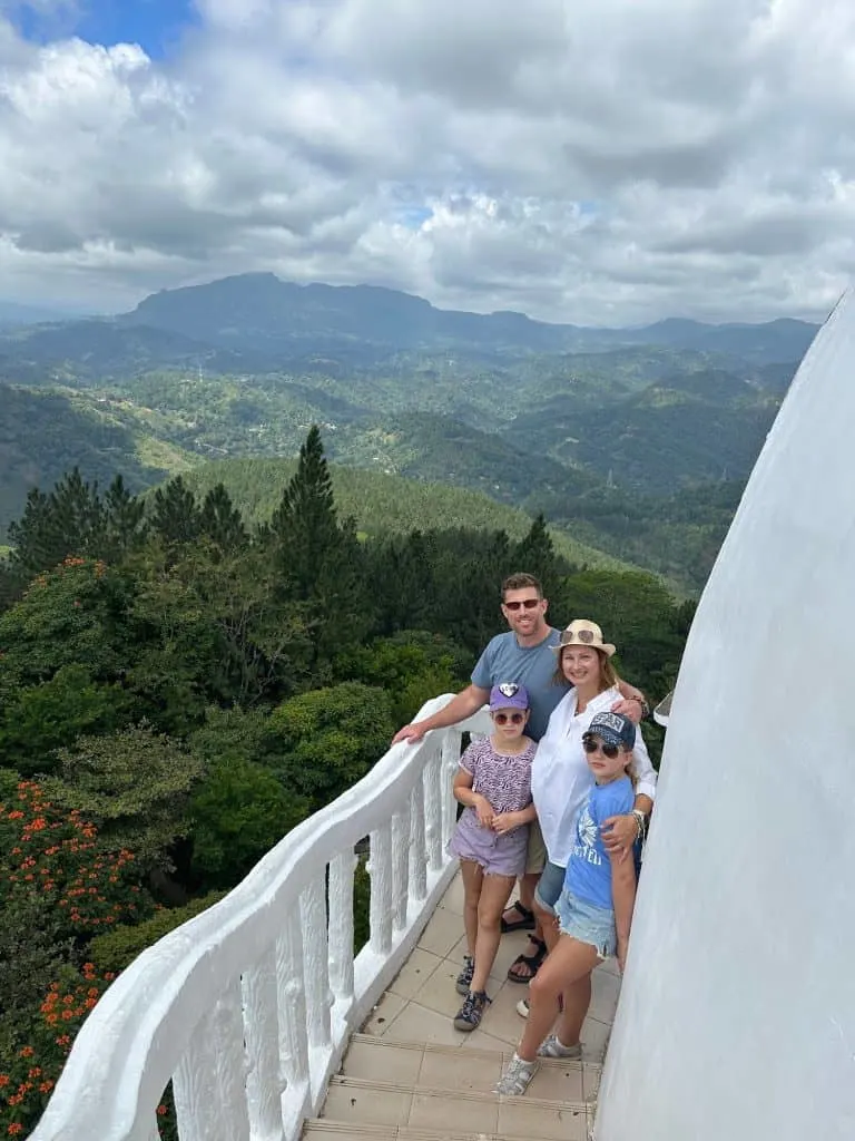 Tin Box family stood on the external steps of Ambuluwawa Tower with a view of the countryside behind them
