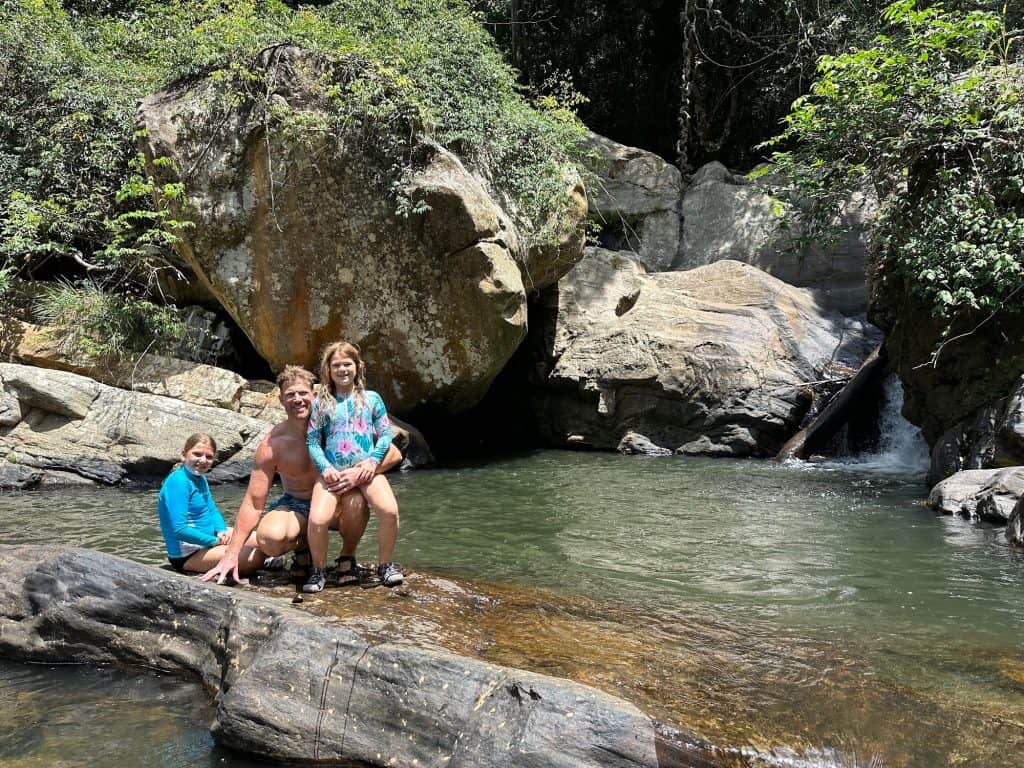 Mr Tin Box and daughters sat on rocks beside a waterfall